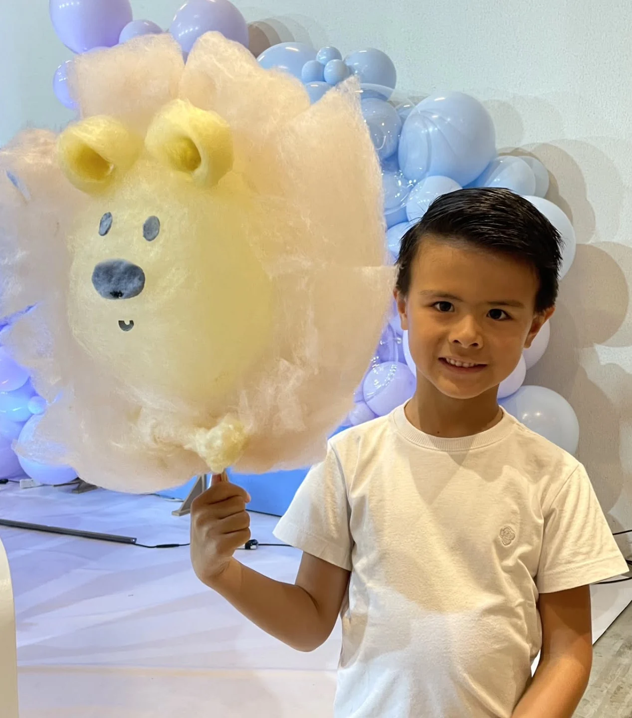 Menino sorrindo com um urso amarelo de algodão-doce