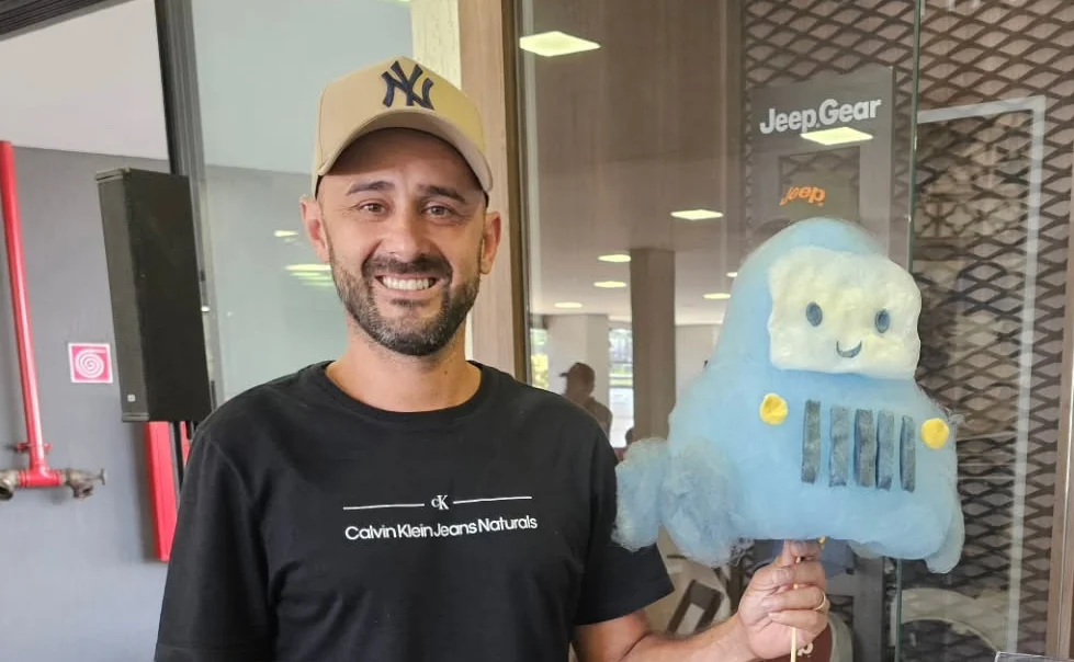 Convidado sorrindo com uma escultura de algodão-doce em forma de jipe, em evento de empresa